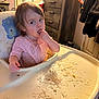 toddler, child, high_chair, spaghetti, messy, pink_onesie, finger_in_mouth, indoor, furniture, cabinet, clothing, tray, meal_time, food, cute, mess, portrait, baby, feeding, room