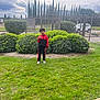 Ayser participe au concours pour gagner de l'argent avec cette photo : child, boy, grass, bush, fence, outdoor, cloudy_sky, tracksuit, white_shoes, greenery, nature, smiling, gesture, daylight, urban, park, casual_clothing, person, standing, happy