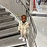 toddler, child, stairs, railing, indoor, modern_building, marble_floor, jacket, pants, sneakers, curious, standing, person, urban, metal, handrail, floor, corridor, shopping_mall, casual_clothing