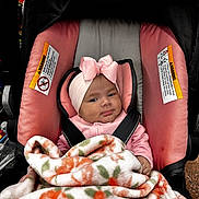 Lizbeth is registered to the contest to win money with this photo: baby, infant, car_seat, blanket, pink, headband, bow, clothing, child, cute, face, person, seatbelt, indoors, soft, warm, smile, portrait, young, bundle