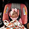 baby, infant, car_seat, blanket, pink, headband, bow, clothing, child, cute, face, person, seatbelt, indoors, soft, warm, smile, portrait, young, bundle