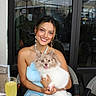woman, person, dog, puppy, fluffy, small_dog, smiling, tongue_out, portrait, outdoor, cafe, restaurant, patio, table, marble, chair, jewelry, dress, drink, ferris_wheel