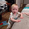 David is registered to the contest to win money with this photo: baby, blanket, book, child, couch, curious, face, floor, furniture, hand, home, indoor, living_room, monitor, pajamas, person, standing, table, toddler, wood_floor