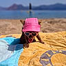 dog, beach, sunglasses, pink_visor, towel, sunny, outdoor, sand, water, mountains, summer, pet, tongue_out, fun, vacation, relaxation, cute, animal, sunshine, canine