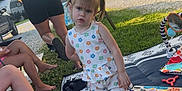 Gabriella is registered to the contest to win money with this photo: child, toddler, outdoor, picnic_blanket, toy, person, grass, tree, campground, trailer, adult, footwear, sitting, sunlight, summer, playtime, pigtails, clothing, barefoot, relaxing