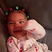 Solana W. joined the competition — help win amazing prizes! baby, child, pajamas, cherry_pattern, smiling, happy, hair_clips, flower_clips, indoors, blanket, couch, cute, infant, cozy, playful, portrait, face, hand, person, relaxing