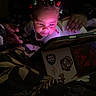 baby, child, tablet, adult, bed, remote_control, hair_clips, flower_clips, glowing_screen, dark_room, focus, curiosity, hand, clothing, blanket, technology, parent, indoor, nighttime, light