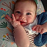 baby, infant, face, blue_eyes, smile, hand, striped_clothing, blanket, cushion, dinosaur_pattern, cute, child, portrait, closeup, indoors, soft_lighting, happy, young, person, skin