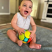 Isaac joined the competition — help win amazing prizes! baby, child, smiling, toy, ball, indoor, blanket, happy, sitting, infant, cute, playful, person, floor, casual_clothing, home, young_child, bright_colors, portrait, fun