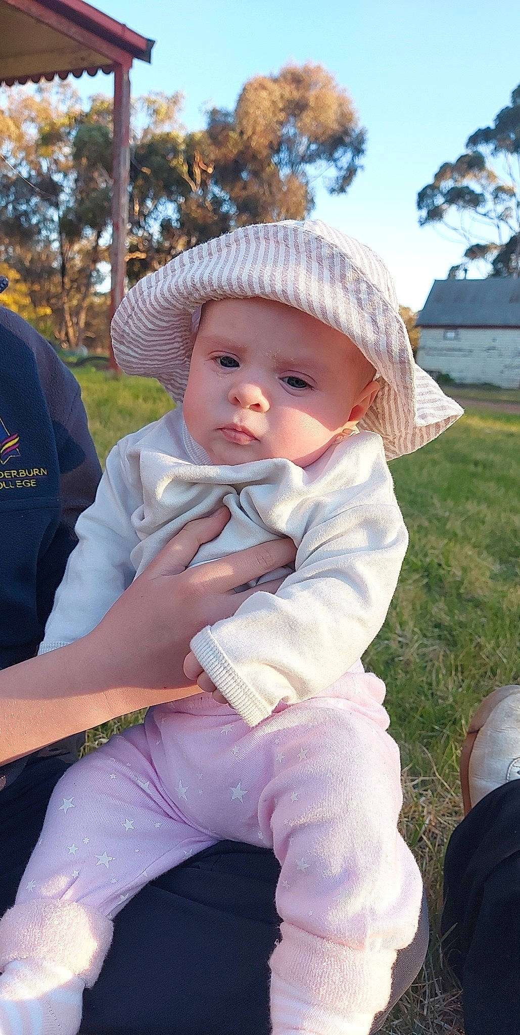 Cassidy is registered to the contest to win money with this photo: baby, cap, child, event, eye, fashion_accessory, fun, grass, happy, headwear, leaf, leisure, people_in_nature, person, pink, plant, sitting, sky, sun_hat, toddler