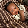 baby, infant, child, blanket, striped_blanket, onesie, star_pattern, sleepwear, face, hand, skin, hair, lying_down, indoors, couch, comfort, curious, expression, closeup, portrait