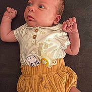 Hugo participe au concours pour gagner de l'argent avec cette photo : baby, infant, pacifier, white_shirt, mustard_shorts, buttoned_clothing, cute, lying_down, indoors, soft_lighting, skin, face, hands, legs, expression, child, newborn, clothing, baby_sock, curious