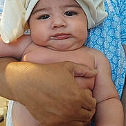 Tevita is registered to the contest to win money with this photo: baby, infant, towel, diaper, hand, adult, blue_clothing, floral_pattern, skin, face, expression, indoor, person, holding, cute, chubby, milk, portrait, child, closeup