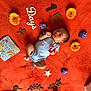 baby, newborn, orange_blanket, yellow_flower, purple_flower, wooden_letters, wooden_numbers, card, hello_little_man, soft_toy, infant, lying_down, decorative_elements, colorful, cute, cozy, peaceful, indoors, portrait, celebration
