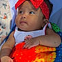 baby, headband, red_bow, blanket, knitted, colorful, infant, child, cute, portrait, hand, clothing, sleeping_area, soft_light, indoors, face, young_child, peaceful, curious, resting