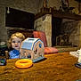 toddler, child, toy, wooden_table, barn_puzzle, orange_ring, curly_hair, indoor, fireplace, stone_wall, chair, television, furniture, rustic, playtime, person, home, cozy, wood, curious