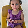 toddler, child, curly_hair, purple_outfit, yellow_chair, serious_expression, sitting, toy, indoor, person, portrait, casual_clothing, young_child, bright_colors, cute, curious, small_hands, buttoned_top, skin, face