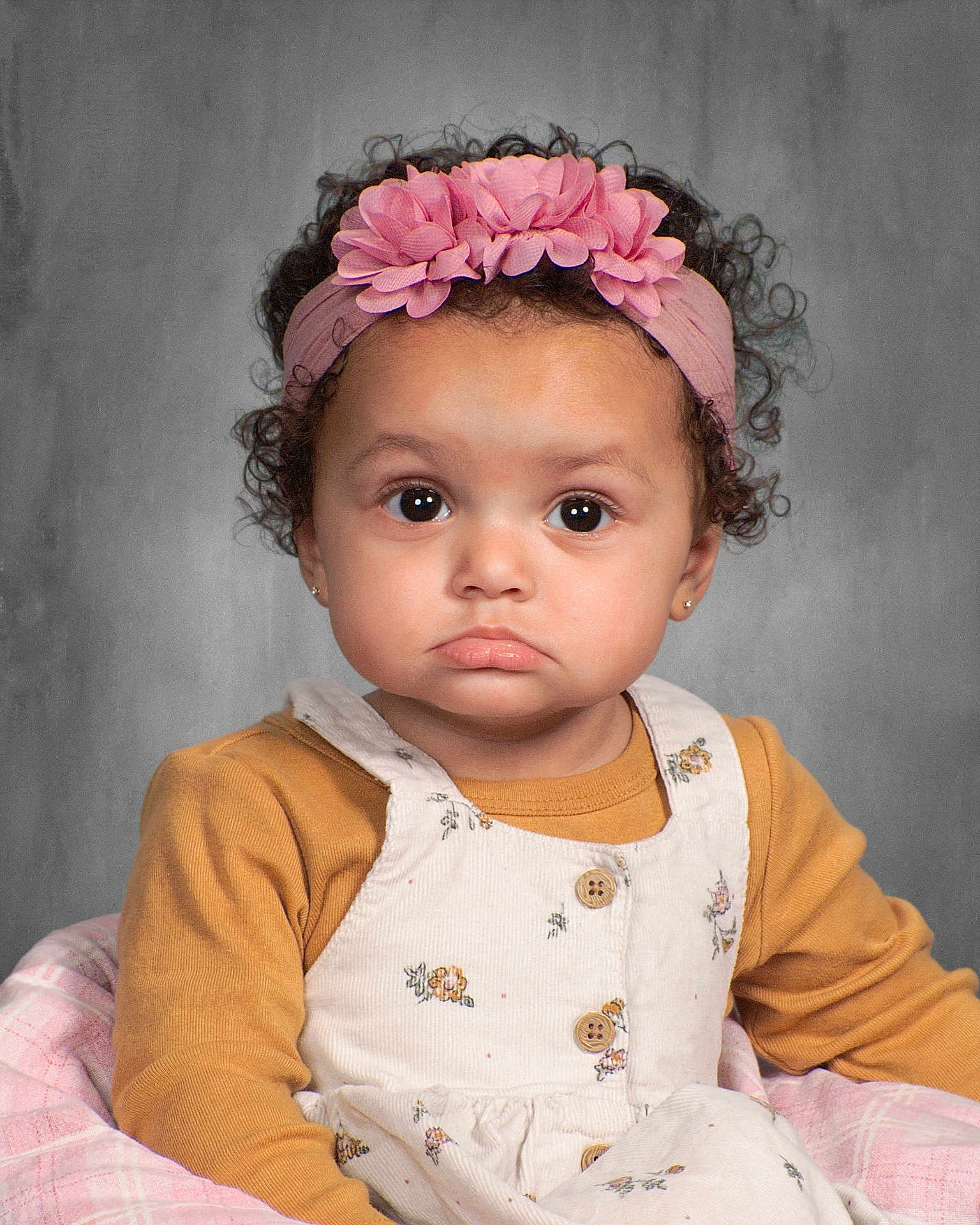 Eliana joined the competition — help win amazing prizes! toddler, child, face, headband, pink, flower, curly_hair, mustard, long_sleeve, dress, buttons, floral_pattern, portrait, studio, expression, pout, cute, person, seated, blanket