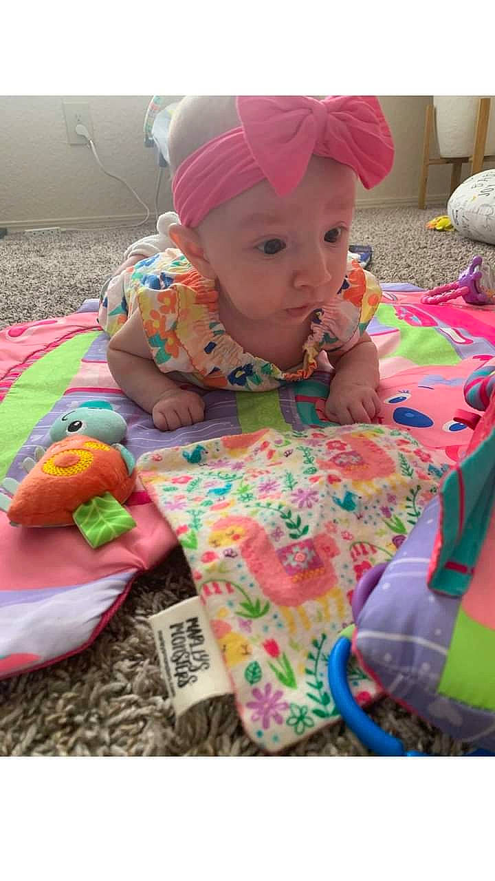 Elianna is registered to the contest to win money with this photo: baby, baby_products, baby_toddler_clothing, cap, child, fun, grass, headwear, linens, orange, pattern, person, pink, play, product, sitting, skin, sleeve, t_shirt, textile