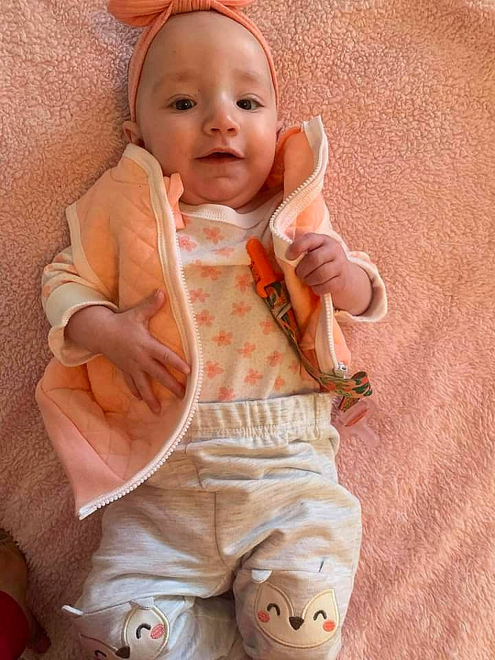 Elianna is registered to the contest to win money with this photo: baby, baby_toddler_clothing, cheek, collar, comfort, face, finger, human_body, mouth, neck, nose, orange, outerwear, person, pink, product, skin, sleeve, smile, textile