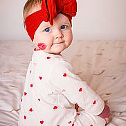 June participe au concours pour gagner de l'argent avec cette photo : baby, child, blue_eyes, red_headband, red_bow, lipstick_mark, heart_pattern, white_outfit, bed, blanket, cute, portrait, sitting, indoor, infant, soft_lighting, looking_back, smile, adorable, cozy