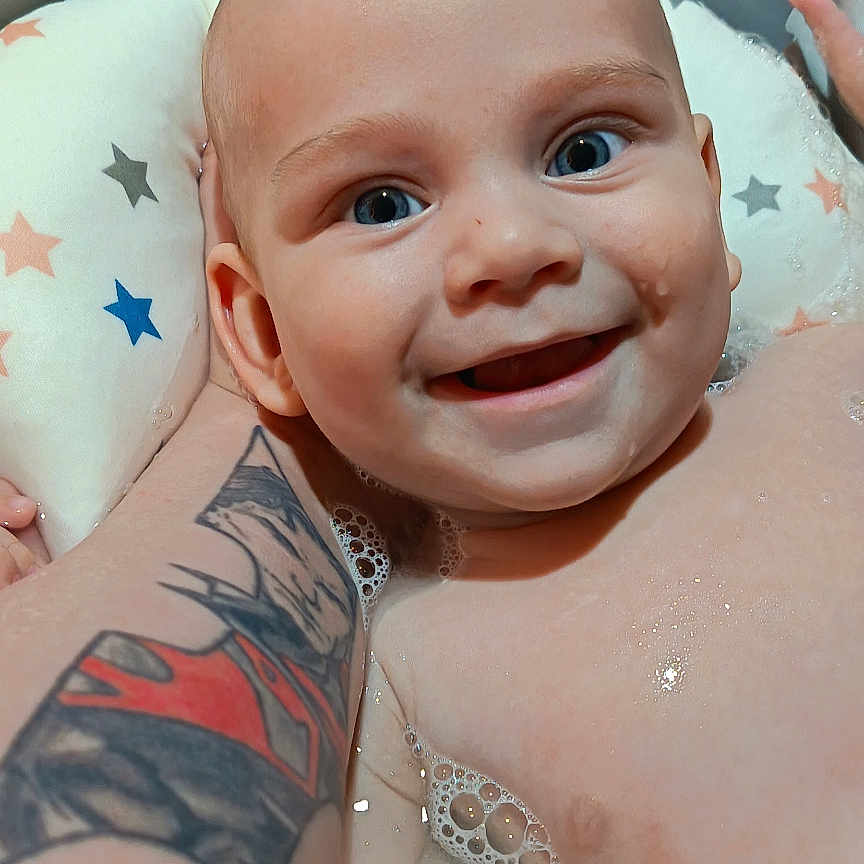 Leo a rejoint le concours — aidez-le/la à gagner de superbes lots ! baby, smiling, bath, water, bubbles, tattoo, arm, cushion, stars, blue_eyes, child, infant, happy, skin, person, indoor, closeup, support, parent, care