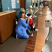 Jordan joined the competition — help win amazing prizes! hospital, woman, dog, scrubs, medical_equipment, hallway, flooring, affection, hug, uniform, leash, celebration, staff, indoor, smile, person, animal, black_and_white, clothing, wood_floor