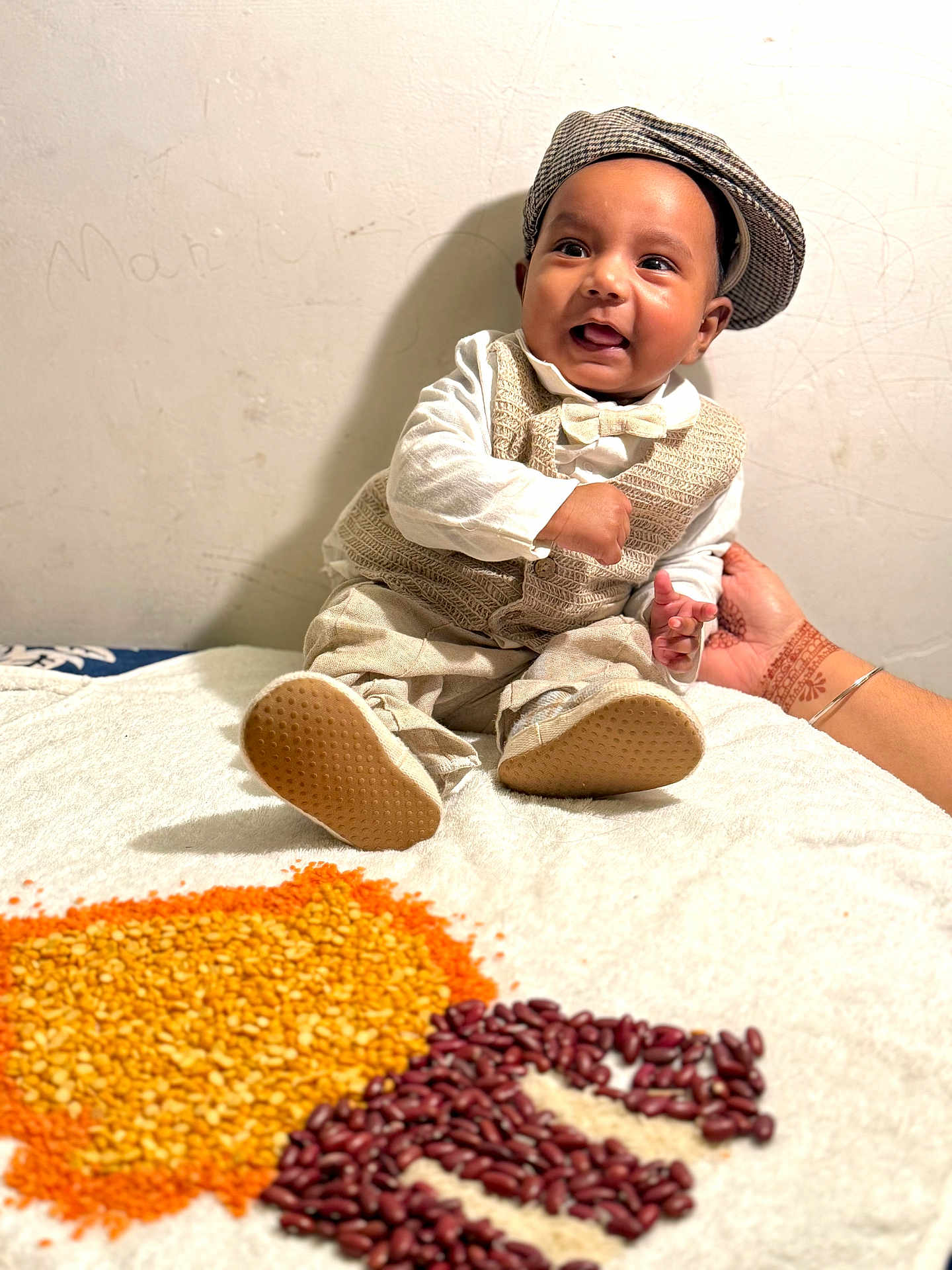 Gurniwaz joined the competition — help win amazing prizes! baby, child, smiling, sitting, hat, vest, bow_tie, hand, adult_hand, bracelet, henna, lentils, beans, blanket, indoors, wall, footwear, portrait, happy, clothing