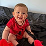 baby, bed, black_socks, child, clothing, cute, face, happy, head, indoor, infant, person, playing, plush_toy, portrait, red_onesie, sitting, skin, smiling, young