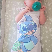 Aiyana is registered to the contest to win money with this photo: baby, infant, pacifier, onesie, cartoon_character, stitch, lying_down, heart_pattern, mattress, cute, sleepwear, hands_near_face, soft_lighting, indoors, newborn, child, sleeping_area, fabric, peaceful, small