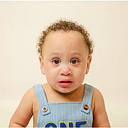 Isaac is registered to the contest to win money with this photo: toddler, child, curly_hair, blue_overall, expression, face, portrait, one_year_old, skin, eyes, mouth, button, clothing, studio, innocent, young, person, cute, background, isolated