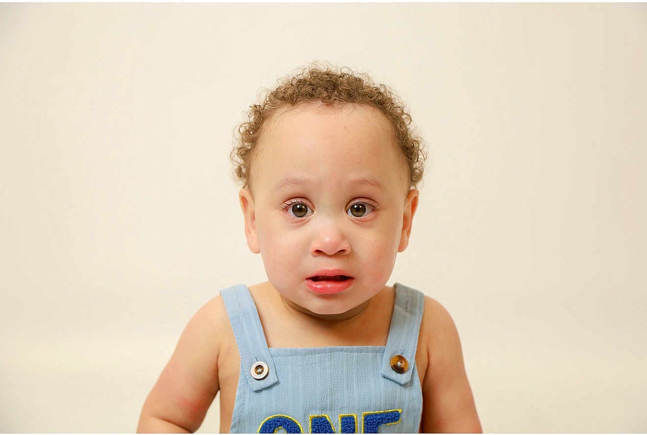 Isaac is registered to the contest to win money with this photo: toddler, child, curly_hair, blue_overall, expression, face, portrait, one_year_old, skin, eyes, mouth, button, clothing, studio, innocent, young, person, cute, background, isolated