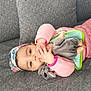 baby, child, couch, gray, pink_clothing, headband, toy, doll, elephant_toy, infant, lying_down, indoors, cute, soft_toy, colorful, hands, face, eyes, cozy, relaxed