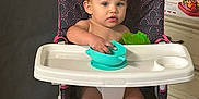 Jay Oliver is registered to the contest to win money with this photo: toddler, child, high_chair, indoor, baby, feeding, bowl, plastic_bowl, pink, black, patterned, face, expression, feet, hands, furniture, floor, cardboard_box, container, person