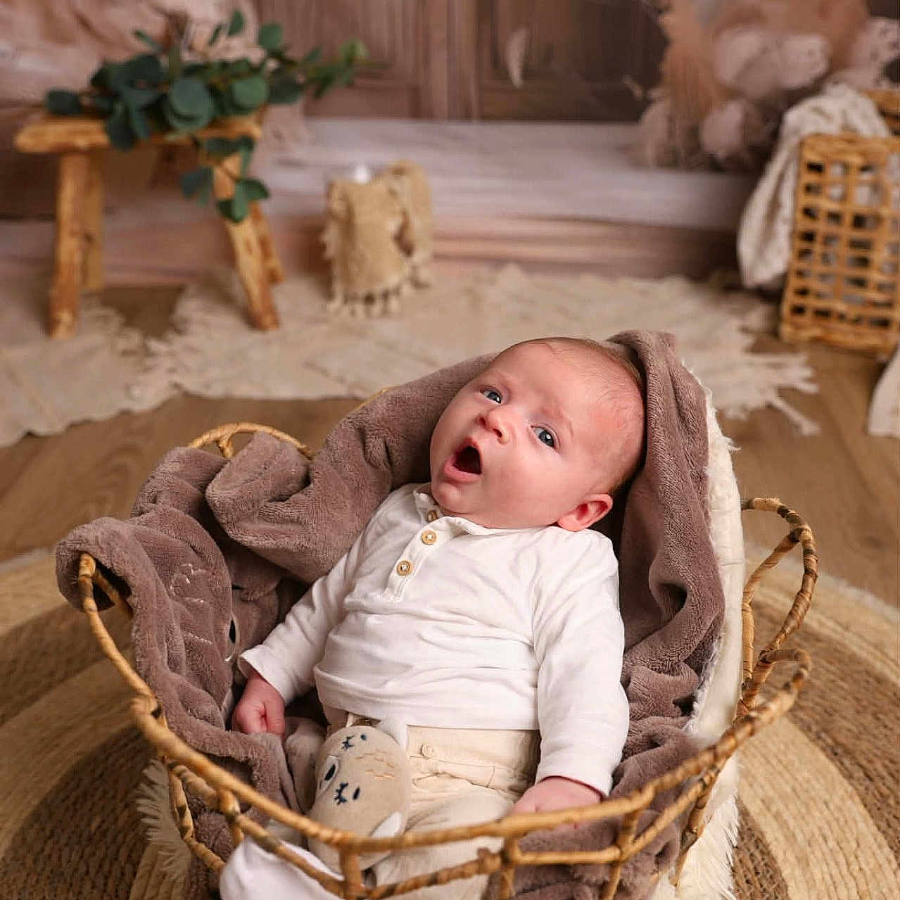 Thélyo a rejoint le concours — aidez-le/la à gagner de superbes lots ! baby, infant, basket, blanket, brown, white_clothing, expression, surprised, wicker, rug, wood_floor, decor, plant, soft_texture, indoors, child, cute, portrait, cozy, nursery