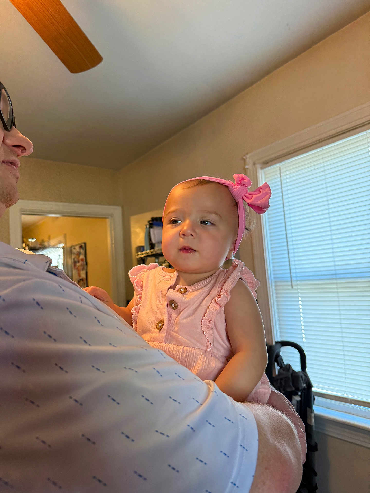 Lizzy is registered to the contest to win money with this photo: toddler, child, baby, pink_dress, headband, adult, indoor, window, blinds, light, person, holding, face, curious, smile, home, family, soft_light, casual, portrait
