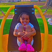 Scarlette is registered to the contest to win money with this photo: child, smiling, swing, playground, outdoor, grass, trees, braided_hair, pink_shoes, sunny, happy, seat, park, daytime, fence, casual_clothing, nature, play, person, fun