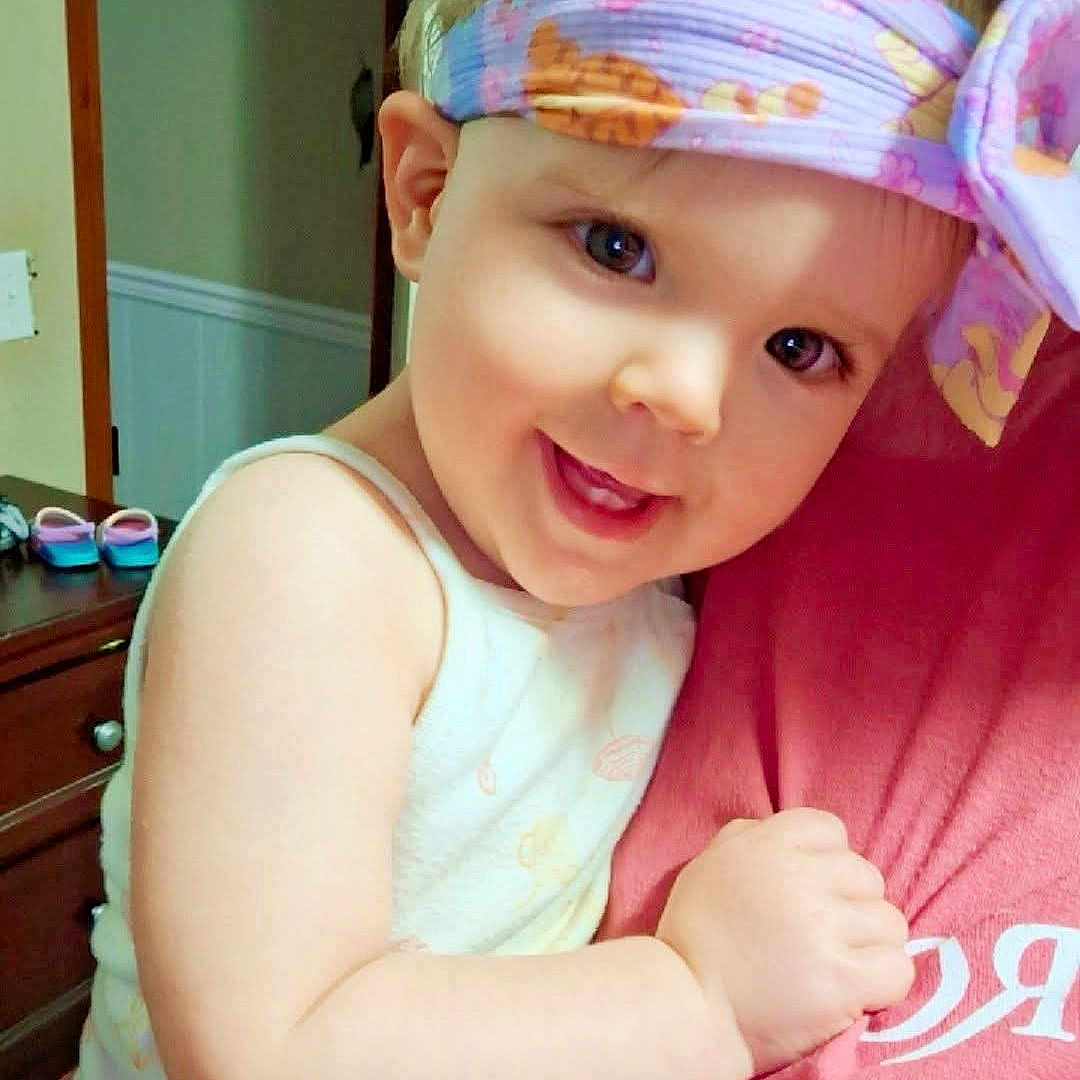 Ivie is registered to the contest to win money with this photo: baby, child, infant, smiling, happy, portrait, headband, floral, colorful, indoor, home, hugging, adult, person, face, eyes, white_clothing, pink_shirt, dresser, shoes