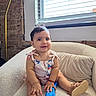 baby, child, smiling, armchair, cookie, oreo, window, blinds, brick_wall, footwear, sandals, jewelry, bracelet, necklace, indoor, cozy, cute, person, happy, portrait