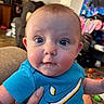 baby, background, blue_shirt, child, clothing, cute, expression, face, hand, holding, home, human, indoor, infant, living_room, person, seated, skin, toy, wide_eyes
