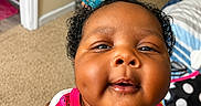 Jhené is registered to the contest to win money with this photo: baby, child, smiling, face, curly_hair, topknot, colorful_clothing, watermelon_pattern, banana_pattern, indoor, carpet, towels, shelf, bed, blanket, hand, person, cute, portrait, happy