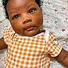adorable, baby, blanket, child, close_up, curly_hair, cute, eyes, face, heart_pattern, hello_kitty, infant, lying_down, onesie, orange_checkered, portrait, skin, smiling, soft_texture, young