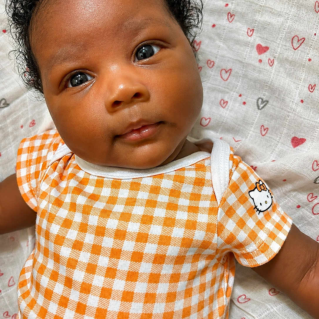 Jhené is registered to the contest to win money with this photo: adorable, baby, blanket, child, close_up, curly_hair, cute, eyes, face, heart_pattern, hello_kitty, infant, lying_down, onesie, orange_checkered, portrait, skin, smiling, soft_texture, young