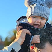 Matías joined the competition — help win amazing prizes! baby, child, hat, knit_hat, pom_poms, smiling, happy, person, adult, glasses, outdoor, blue_sky, hand, face, jacket, warm_clothing, portrait, family, playful, daylight