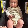 baby, infant, child, portrait, car_seat, football, football_outfit, onesie, sitting, wide_eyed, face, hands, legs, indoor, safety_labels, black_background, close_up, adorable, photography, family