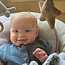 baby, infant, child, smiling, portrait, indoor, sitting, blue_clothing, onesie, plush_toys, stuffed_animals, star_toys, nursery, bed, blanket, window, natural_light, happy, face, closeup