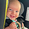 baby, infant, child, smiling, car_seat, harness, vehicle, interior, portrait, face, happy, drool, toy, hands, sitting, travel, safety_label, close_up, daylight, photography