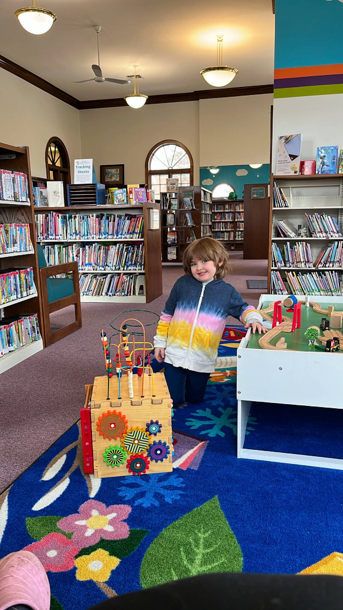 Evelyn is registered to the contest to win money with this photo: book, bookcase, building, chair, child, event, flooring, furniture, interior_design, joy, library, lighting, person, play, publication, retail, room, shelf, shelving, table