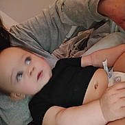 Kason is registered to the contest to win money with this photo: baby, infant, black_shirt, diaper, arm, person, skin, face, hand, lap, clothing, indoor, blur, casual, resting, child, human, adult, grey_sleeve, curious_expression