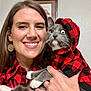 casual, cat, cozy, cute, earrings, funny_eye, gray_cat, hand, happy, holding, hoodie, indoor, long_hair, matching_outfits, pet, portrait, red_and_black_checkered, smiling, white_paws, woman